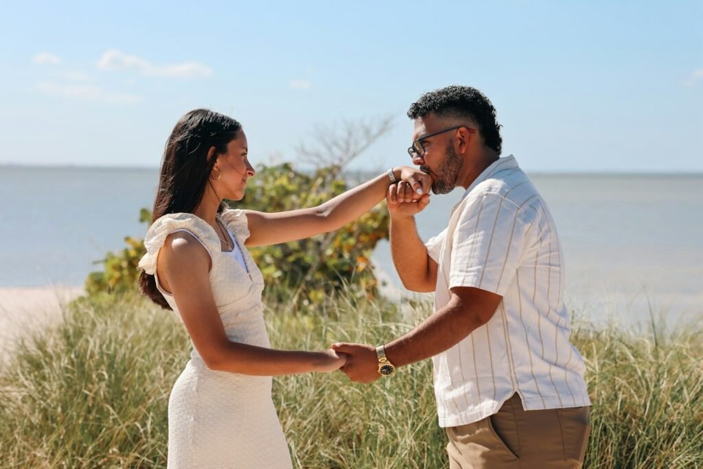 Man kisses woman's hand on a sunny beach.