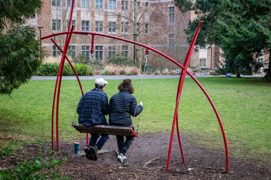 Two people sit on a park swing.