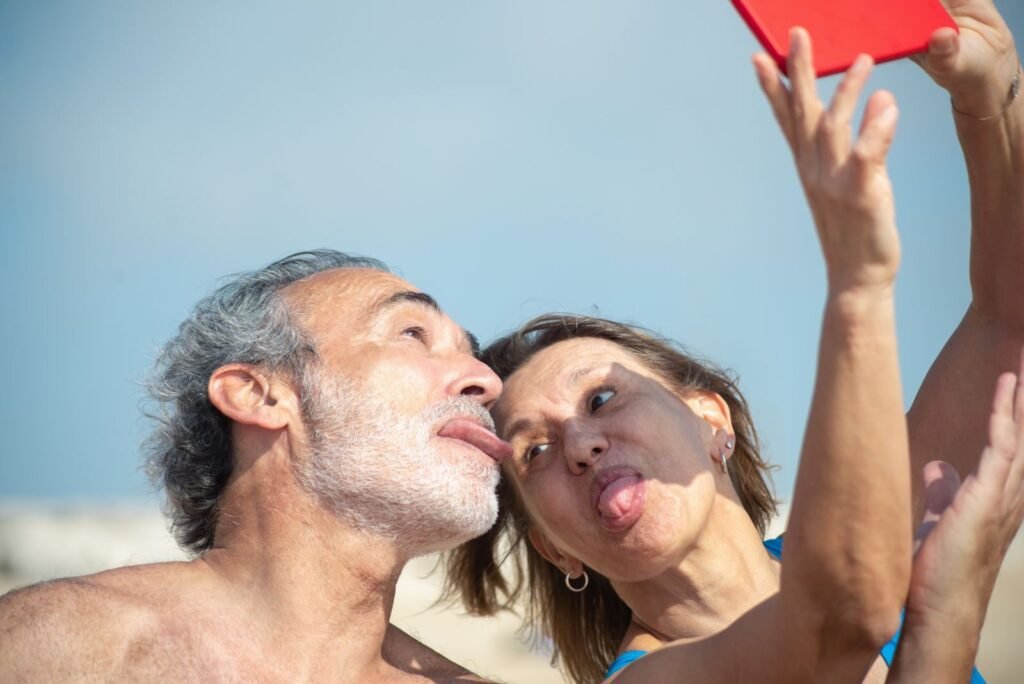 Elderly couple enjoying a fun selfie moment on a sunny beach in Portugal.