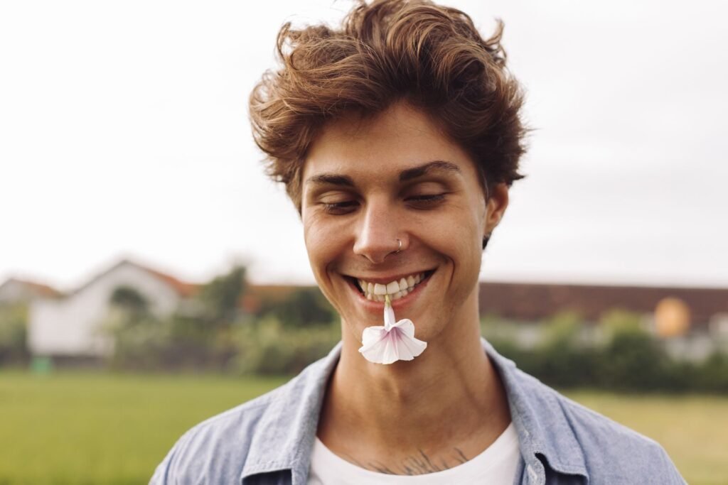 Young man smiling with a flower in his mouth, enjoying an outdoor setting.