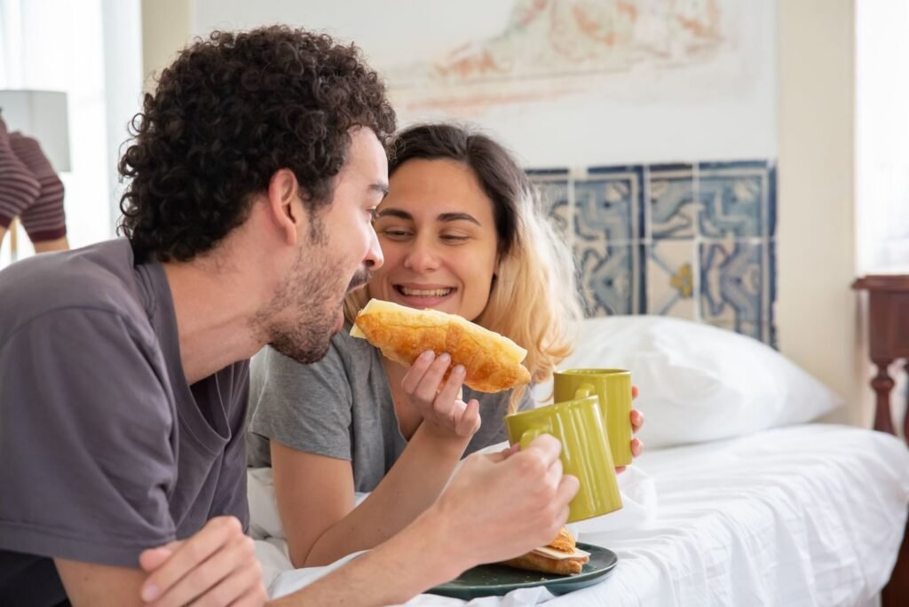A loving couple enjoys breakfast in bed with croissants and coffee, showcasing warmth and romance.
