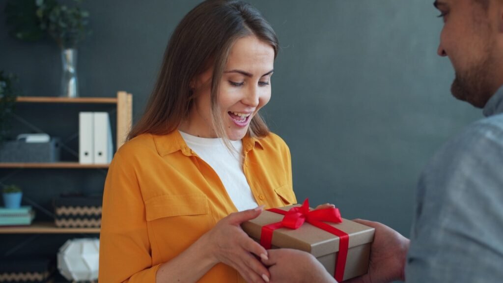Man gives woman a wrapped gift with red ribbon.